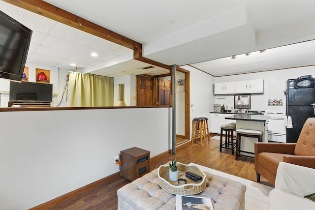 living room featuring a paneled ceiling, dark wood-style flooring, baseboards, and recessed lighting
