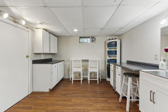 kitchen featuring a paneled ceiling, dark countertops, dark wood-type flooring, and white cabinets