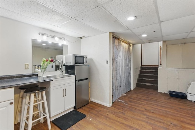 interior space with a drop ceiling, wood finished floors, a sink, appliances with stainless steel finishes, and stairs