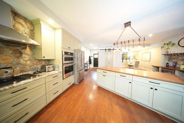 kitchen featuring butcher block countertops, backsplash, light hardwood / wood-style floors, hanging light fixtures, and stainless steel appliances