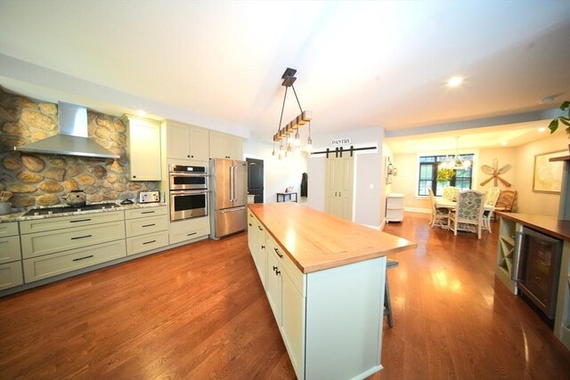 kitchen featuring a kitchen island, wall chimney exhaust hood, beverage cooler, wood-type flooring, and stainless steel appliances