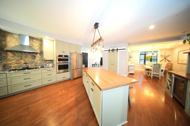 114 Country Club Way, Kingston, MA 02364 - kitchen featuring butcher block countertops, stainless steel appliances, a barn door, wall chimney range hood, and wood finished floors