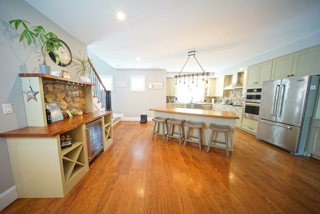 kitchen featuring pendant lighting, stainless steel appliances, wall chimney range hood, wood counters, and light hardwood / wood-style floors