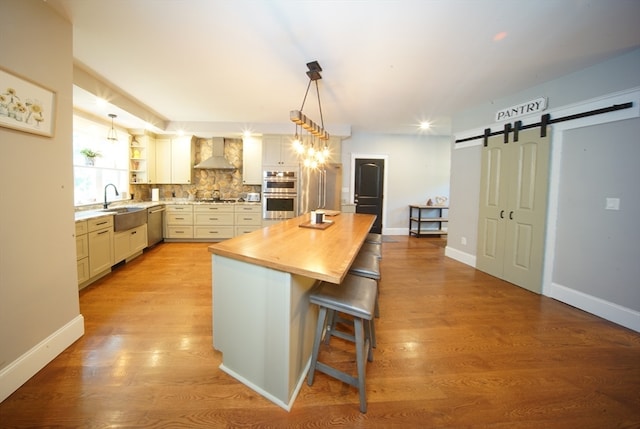 kitchen featuring wall chimney exhaust hood, a breakfast bar, a center island, a barn door, and light wood-type flooring