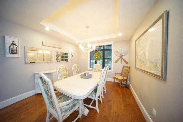 dining space with dark wood-type flooring, a notable chandelier, and a tray ceiling