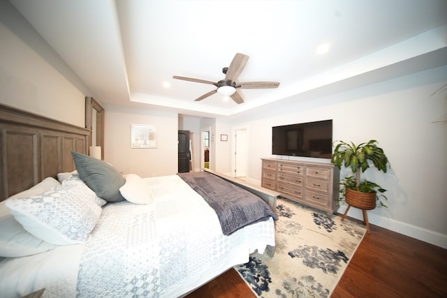 bedroom with dark wood-type flooring, ceiling fan, and a tray ceiling