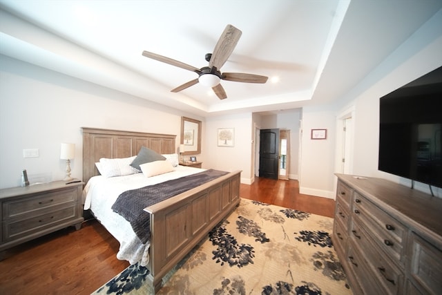 bedroom with dark wood-type flooring, ceiling fan, and a raised ceiling