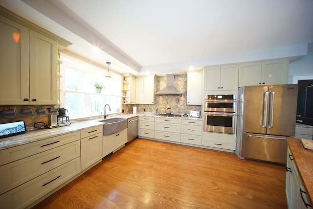 kitchen featuring butcher block counters, stainless steel appliances, wall chimney range hood, sink, and light hardwood / wood-style floors