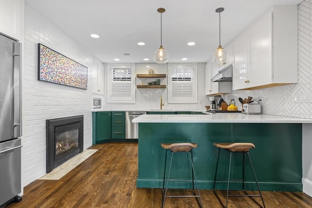 kitchen with dark wood-type flooring, under cabinet range hood, stainless steel appliances, a peninsula, and light countertops