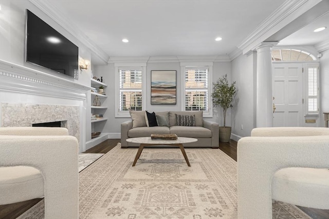 living area featuring decorative columns, baseboards, wood finished floors, and crown molding