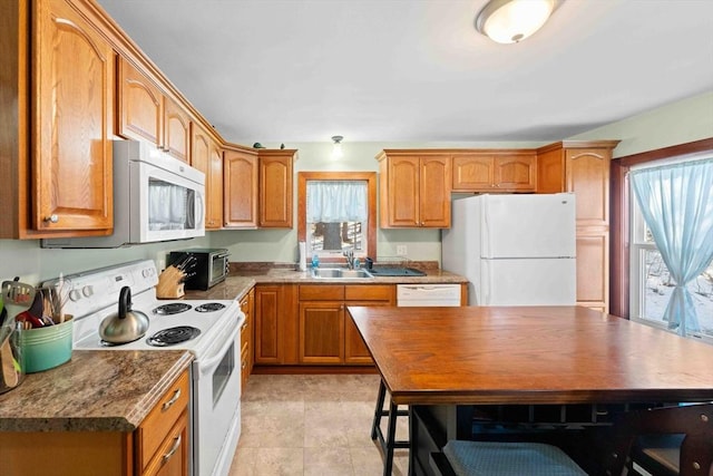 kitchen featuring a wealth of natural light, white appliances, brown cabinetry, and a sink