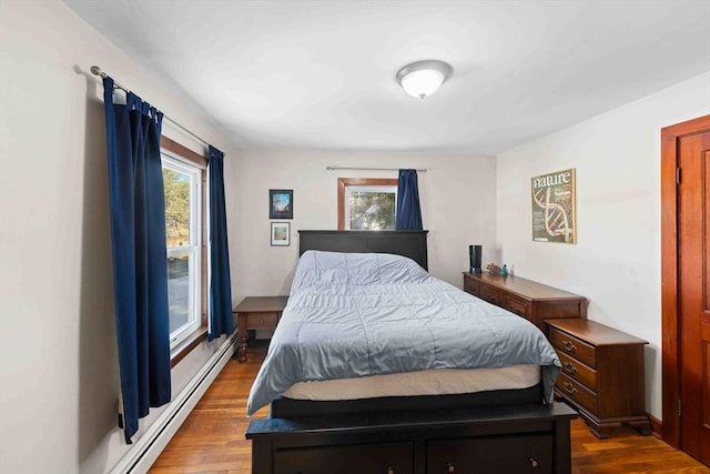 bedroom with baseboard heating, multiple windows, and wood finished floors