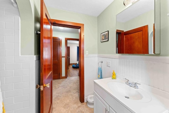 bathroom with vanity, toilet, and a wainscoted wall