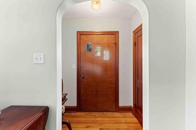 hall featuring light wood finished floors, arched walkways, and baseboards