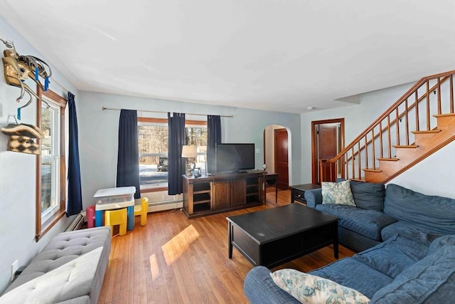 living area featuring stairs, wood finished floors, arched walkways, and a baseboard radiator