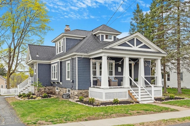 bungalow featuring a porch, a chimney, roof with shingles, stairway, and a front lawn