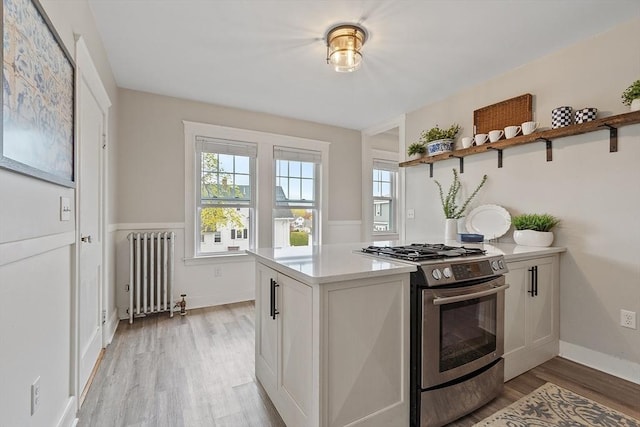 kitchen featuring open shelves, radiator heating unit, plenty of natural light, light wood-type flooring, and stainless steel range with gas stovetop
