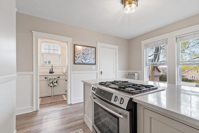 kitchen with stainless steel range with gas cooktop, light wood-style flooring, light stone counters, and radiator heating unit