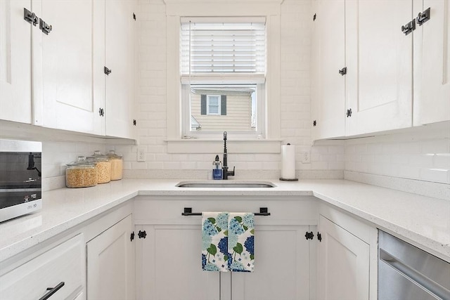kitchen featuring stainless steel dishwasher, backsplash, white cabinetry, and a sink