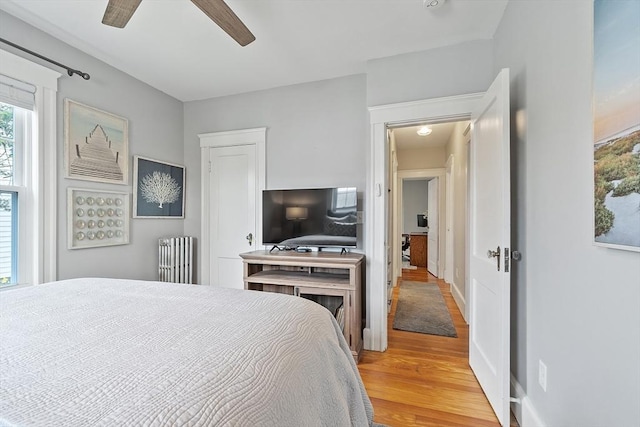 bedroom featuring light wood-style floors, baseboards, ceiling fan, and radiator heating unit