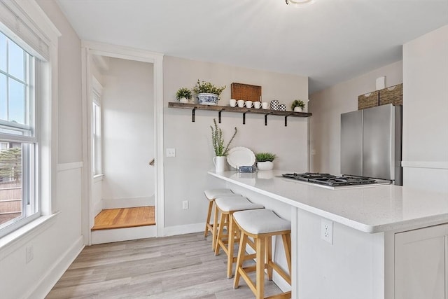 kitchen with appliances with stainless steel finishes, baseboards, open shelves, and light wood-style flooring