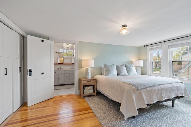 bedroom with connected bathroom, a notable chandelier, and light wood-style floors