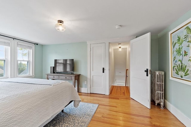 bedroom with radiator heating unit, baseboards, and light wood-type flooring