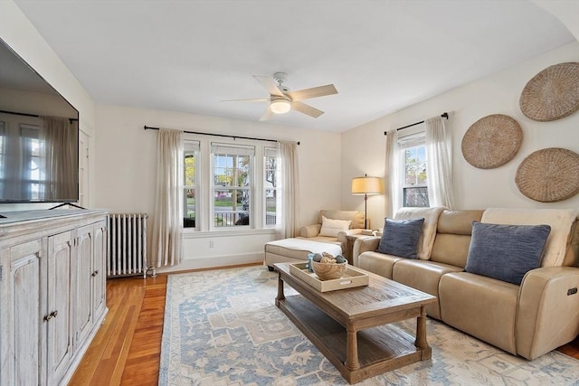 living area with light wood-style floors, a ceiling fan, and radiator heating unit