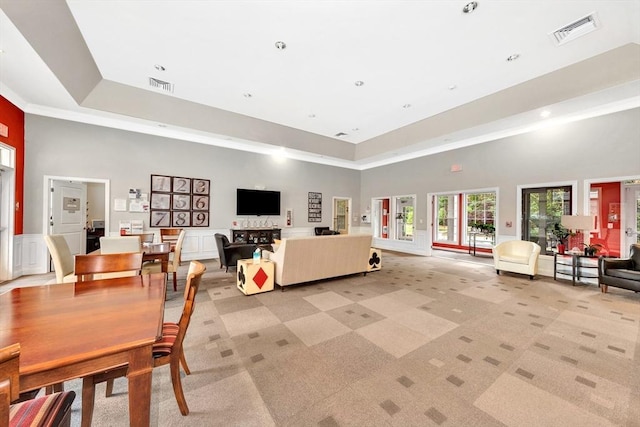 living area featuring visible vents, a raised ceiling, light carpet, and a towering ceiling