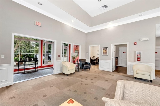 living area featuring a wainscoted wall, visible vents, light carpet, crown molding, and a decorative wall