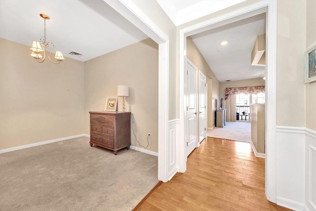 hallway with light wood-type flooring, visible vents, light carpet, an inviting chandelier, and baseboards