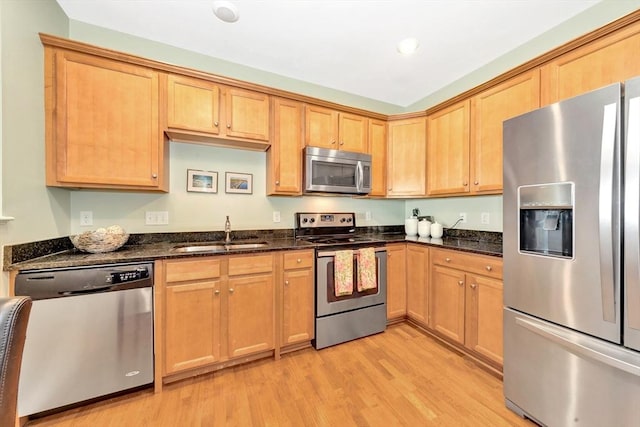 kitchen featuring a sink, dark stone counters, light wood-style flooring, and stainless steel appliances