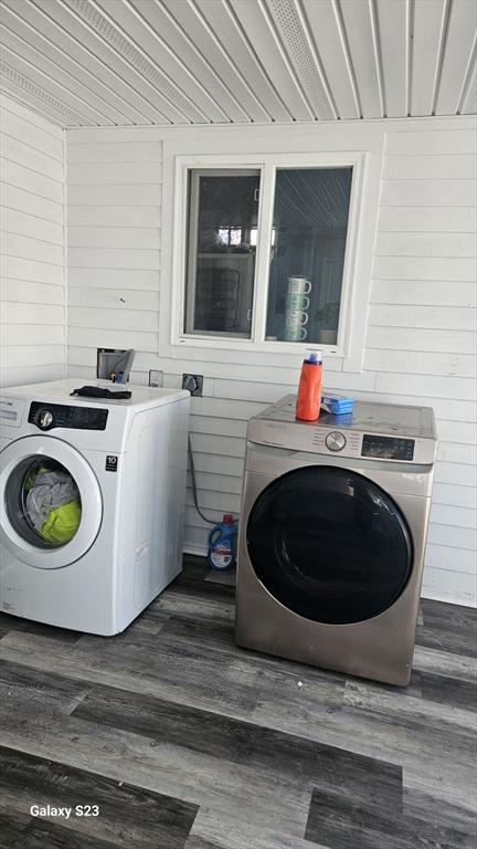 laundry area with laundry area, wooden walls, wood finished floors, and washing machine and dryer