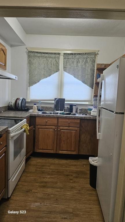 kitchen featuring white appliances, dark countertops, dark wood-type flooring, and a sink