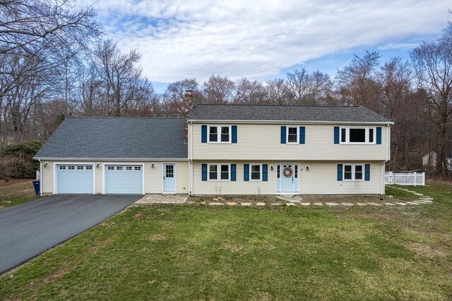 colonial inspired home with fence, a front yard, a chimney, an attached garage, and driveway