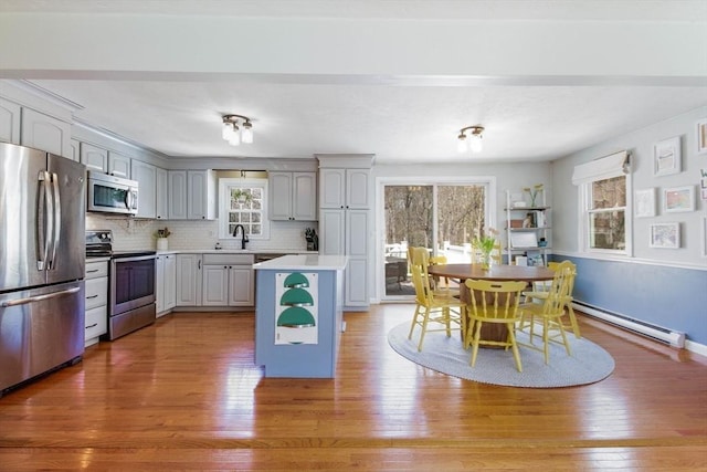 kitchen with stainless steel appliances, a wealth of natural light, baseboard heating, and light wood-style floors