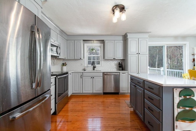 kitchen featuring appliances with stainless steel finishes, tasteful backsplash, light countertops, light wood-type flooring, and gray cabinetry