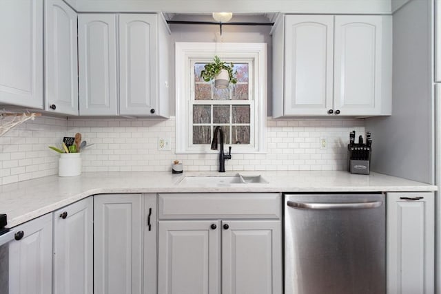 kitchen featuring white cabinets, light stone counters, a sink, tasteful backsplash, and stainless steel dishwasher