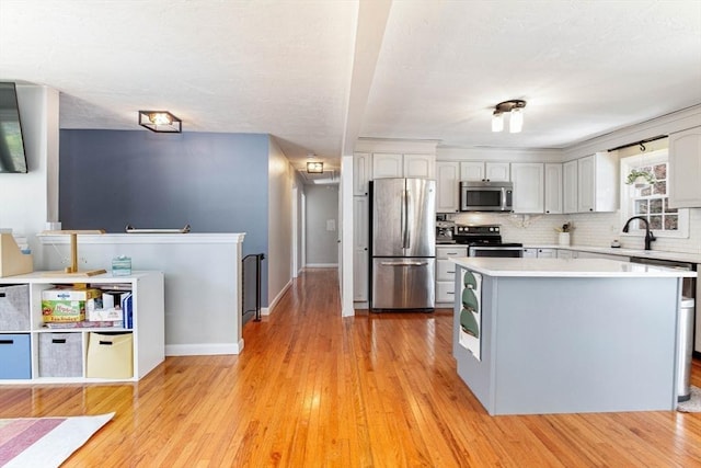 kitchen with a kitchen island, appliances with stainless steel finishes, tasteful backsplash, light countertops, and light wood finished floors