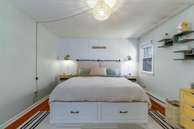 bedroom featuring baseboards, baseboard heating, an accent wall, and light wood-style floors