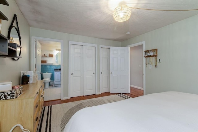 bedroom featuring ensuite bathroom, wood finished floors, a notable chandelier, and two closets