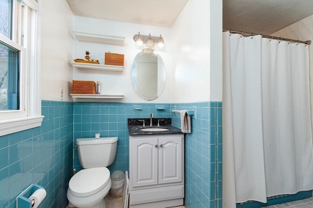 bathroom with a shower with curtain, tile walls, wainscoting, vanity, and toilet