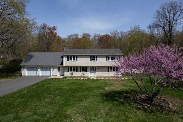 colonial house with an attached garage, a chimney, driveway, and a front yard