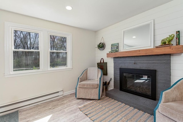 sitting room with baseboards, a baseboard radiator, a brick fireplace, and wood finished floors