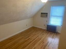 additional living space featuring hardwood / wood-style flooring, an AC wall unit, radiator, and lofted ceiling