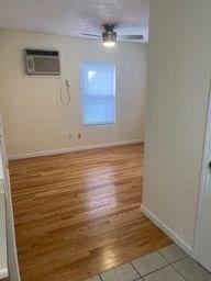 empty room with an AC wall unit, ceiling fan, and light wood-type flooring