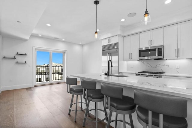 kitchen with white cabinetry, light stone countertops, stainless steel appliances, and sink