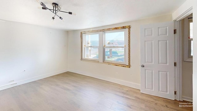 unfurnished room featuring a notable chandelier and light hardwood / wood-style flooring