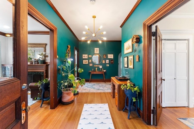 hallway with a notable chandelier, ornamental molding, and light wood-style floors