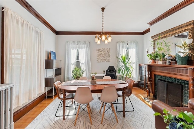 dining space with light wood-style floors, a fireplace, ornamental molding, and a chandelier